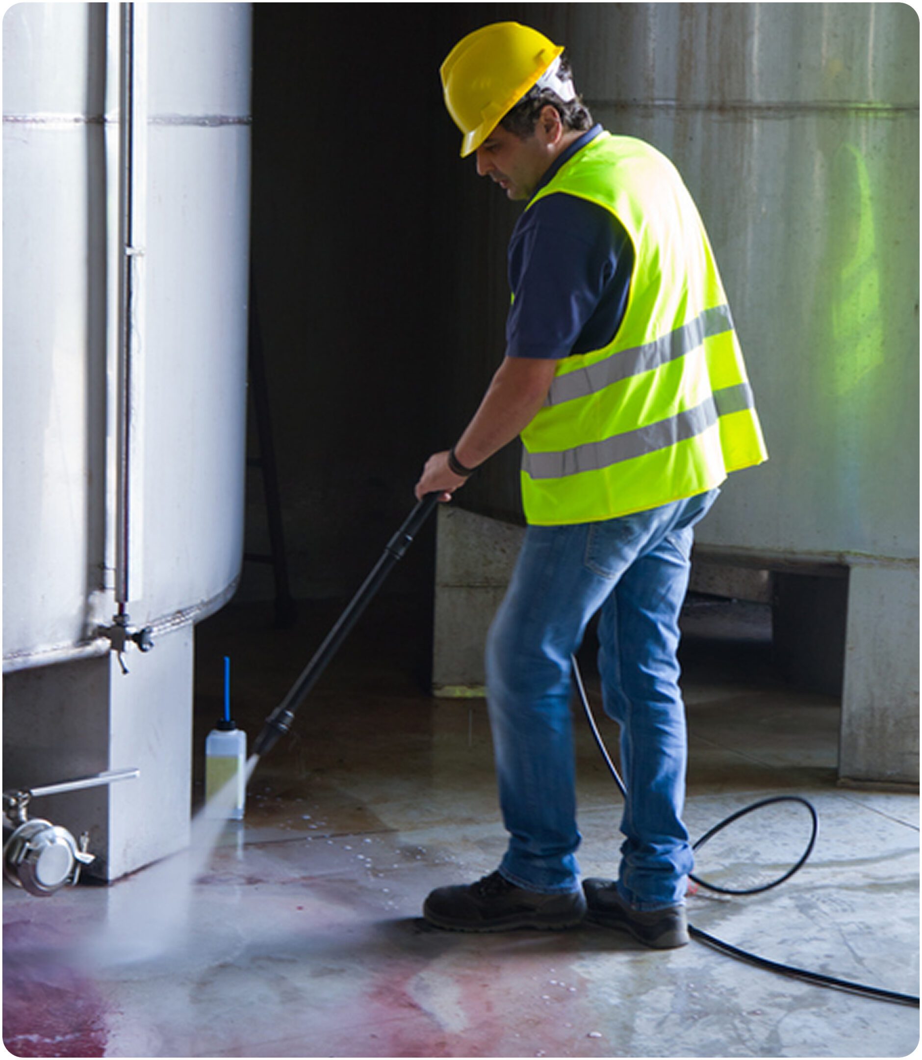 Worker pressure washing industrial tank floor.
